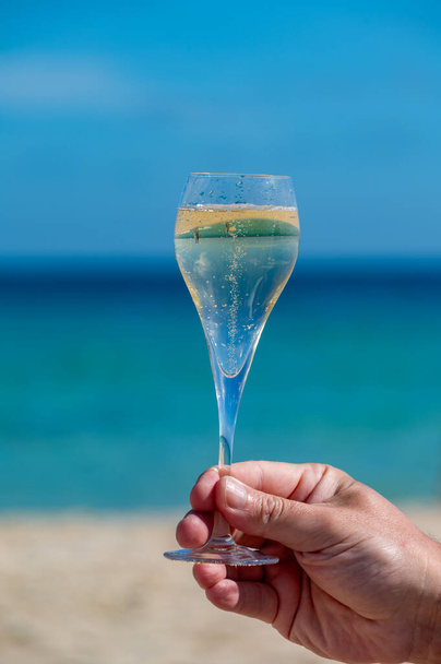 Mano con copa de cava o champán espumoso de vacaciones, Dunas Corralejo Gran playa de arena, Fuerteventura, Islas Canarias, océano azul - Foto, imagen