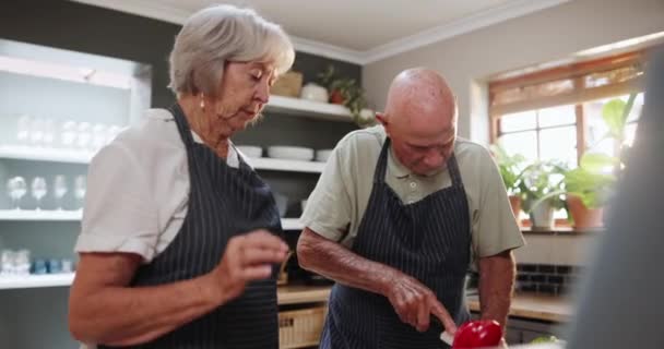 Idős pár, főzés és vágás élelmiszer késsel recept, konyha vagy összetevők a konyhában. Komoly idős férfi és nő kötényben, vacsora, étkezés vagy snack a házban. - Felvétel, videó