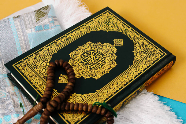 O Alcorão Sagrado com um tapete de oração e tasbih em um fundo azul e amarelo - Foto, Imagem