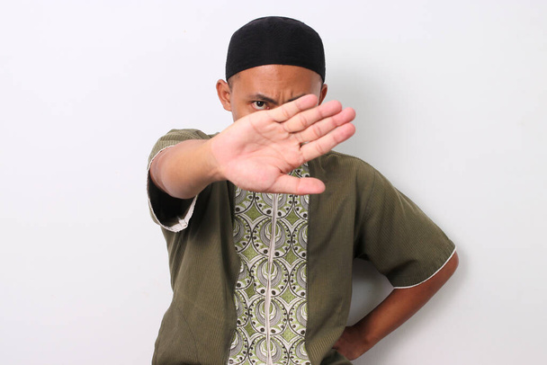 Indonesische moslim man in koko shirt en peci kruist zijn armen in een stop gebaar. Geïsoleerd op witte achtergrond - Foto, afbeelding