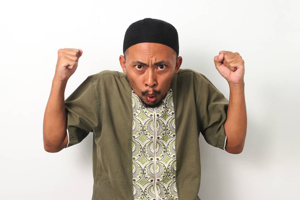 Un musulmán indonesio, levanta el puño sorprendido y emocionado al recibir una oferta inesperada durante el período especial del Ramadán. Aislado sobre fondo blanco - Foto, Imagen