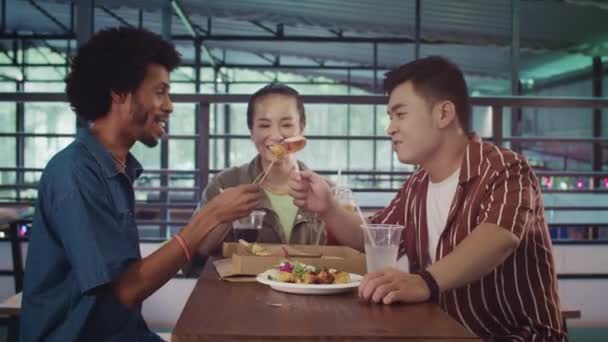Medium shot van multiculturele mensen proeven van straatvoedsel met drankjes in trendy voedselmarkt zitten aan tafel - Video