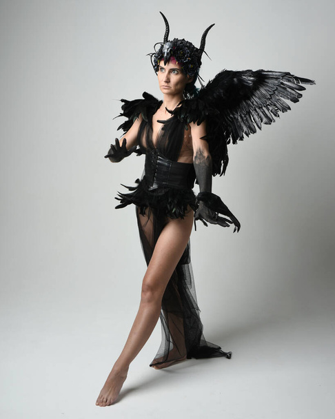 Портрет жіночої моделі з готичним рогатим головним убором з чорною сукнею на Хеллоуїн та крилами фентезійних ангелів. Стоїть пішки, тримає позу пташиного рушія. Ізольований студійний фон - Фото, зображення