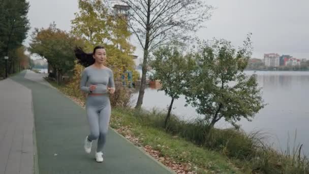 Ázsiai vonzó nő futó képzés a nyári parkban, közel a helyi tó. Fitness Lady Kocog a szabadban. Reggeli futás koncepció. Női tréning kint. Atlétikai Sport Lady Running - Felvétel, videó