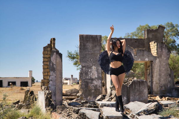 South American woman, young, beautiful, brunette with lingerie and black wings, posing in the middle of the ruins of a building. Concept angels, beauty, costumes, wings, halloween. - Photo, Image