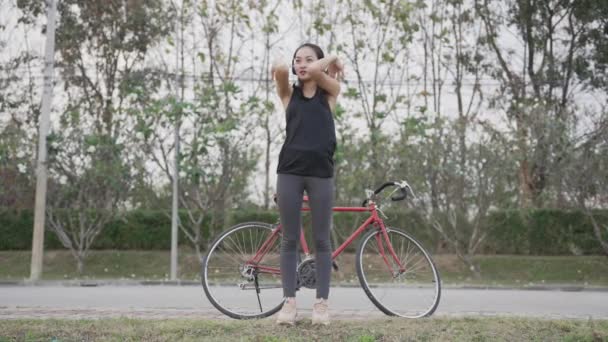 Donna asiatica va felicemente in bicicletta per esercitare nel parco con uno zaino sulla schiena. Video 4K - Filmati, video