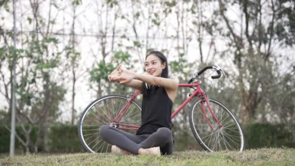 アジアの女性は,彼女の背中のバックパックで公園で運動するために喜んで自転車に乗ります. 4Kビデオ - 映像、動画