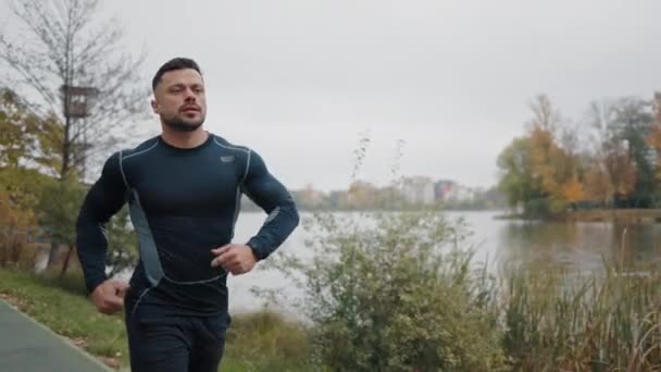 Vonzó férfi, Guy kocog a parkban a fák hátterében. Kaukázusi futó futás. Reggeli Jog Sport Atlétikai Férfi a Fekete Sportruházatban. A helyi tó közelében kocogok. Egészséges életmód - Felvétel, videó