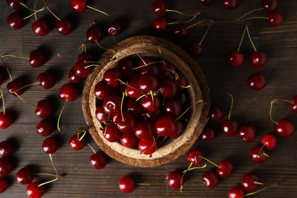 Ripe cherry fruits in a bowl on a wooden background - Photo, Image