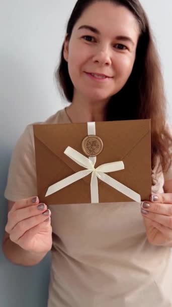Chèque-cadeau en bronze élégante enveloppe dans les mains féminines en beige T-shirt sur fond blanc - Séquence, vidéo