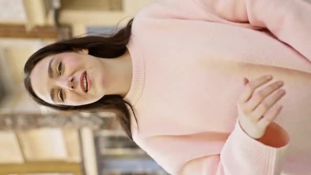 Una joven mujer caucásica en un suéter rosa gestos mientras habla en una calle de la ciudad. - Imágenes, Vídeo