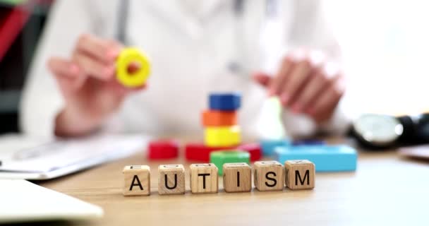 Lääkäri pitää käsissä monivärinen kuutiot ja teksti autismi. Autististen lasten kehitys ja lapsen tilan parantaminen ja sopeutuminen ympäröivään maailmaan - Materiaali, video