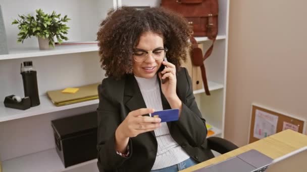 Kıvırcık saçlı genç İspanyol kadın, ofisinde kredi kartıyla konuşuyor.. - Video, Çekim
