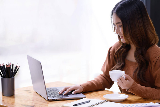 Молода жінка тримає чашку кави, розслабляючись, сидячи за робочим столом в офісі. Бізнес казуальна концепція - Фото, зображення
