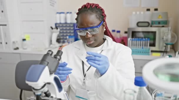 Afrykańska amerykańska naukowiec kobieta analizując próbki za pomocą mikroskopu w laboratorium. - Materiał filmowy, wideo