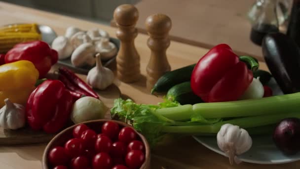 Κοντινό πλάνο βιολογικών φρέσκων ντοματών, πιπεριών, αβοκάντο, σκόρδου, σέλινου, καλαμποκιού και μελιτζάνας σε ξύλινο τραπέζι μαγειρέματος - Πλάνα, βίντεο