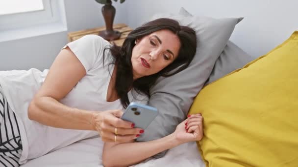 Eine reife hispanische Frau liegt im Bett und interagiert zu Hause im Schlafzimmer mit ihrem Smartphone. - Filmmaterial, Video