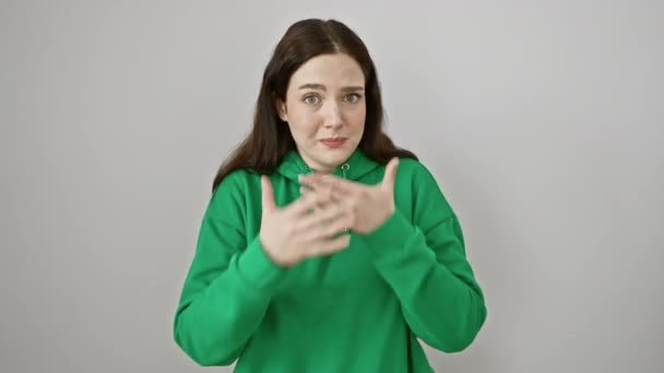 Peekaboo! young woman, clad in sweatshirt on white, her eyes wide with shock, covers blushing face with shy hand peek, expression of embarrassment seeping through finger covering - Footage, Video