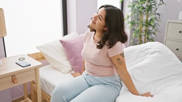 Een jonge Spaanse vrouw ontspant in haar slaapkamer, ademt schoonheid en rust uit temidden van een gezellig interieur. - Video