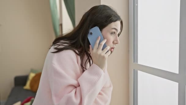 Mujer joven caucásica hablando en un teléfono inteligente en un ambiente interior acogedor - Imágenes, Vídeo