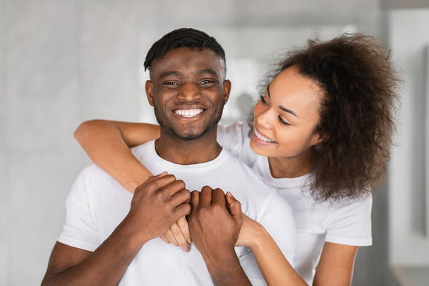 Sevecen Afrikalı Amerikalı çift birbirlerine sarılıp gülümsüyorlar, portre için poz veriyorlar, aile içi tuvaletlerdeki ilişkilerinin neşe ve sevgisini yansıtıyorlar. - Fotoğraf, Görsel