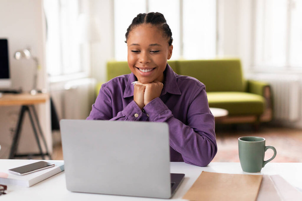 Cheerful african american female student engages in an online class, her smile hinting at the enjoyable and interactive experience of her digital learning environment - Photo, Image