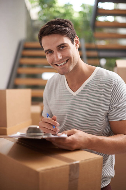 Man, boxes and portrait with clipboard for moving, delivery and documents for logistics, smile and invoice. Person, cardboard and package with paperwork for service, signature and stock in new house. - Photo, Image