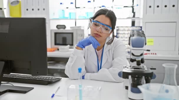 Задумчивая женщина-ученый в лаборатории с микроскопом, компьютером и лабораторным оборудованием. - Кадры, видео