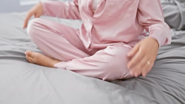 Μια γαλήνια γυναίκα με ροζ πιτζάμες που κάνει διαλογισμό σε ένα άνετο κρεβάτι υπνοδωματίου, αποπνέοντας ηρεμία και σύνεση - Πλάνα, βίντεο