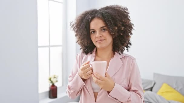 Mosolygó fiatal nő göndör haj élvezi kávé otthon egy hangulatos hálószoba beállítás. - Felvétel, videó