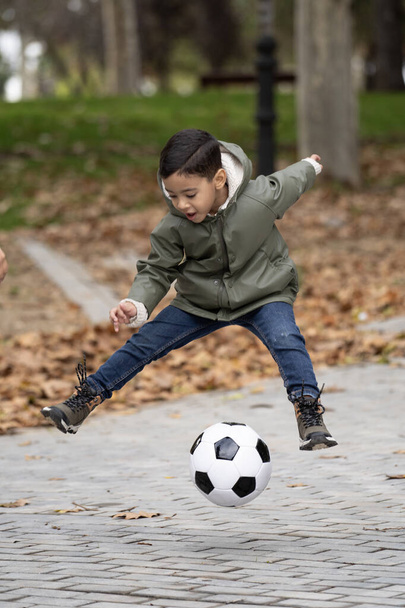 Enfant heureux avec ballon de football sautant dehors dans un parc public. - Photo, image