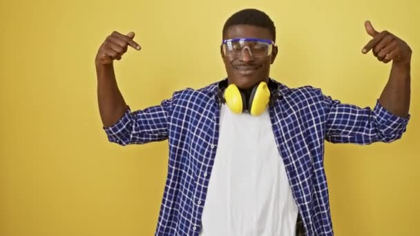 Fiducioso uomo afroamericano con occhiali di sicurezza, che si indica orgogliosamente su sfondo giallo. un esempio promettente di successo, dall'aspetto felice e sicuro di sé. - Filmati, video