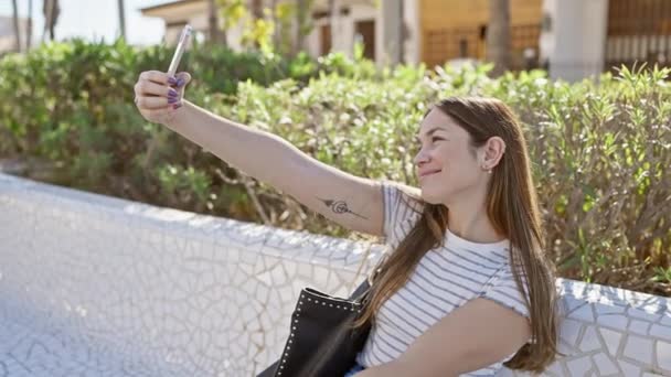 Mujer sonriente tomando selfie en parque soleado con vegetación - Metraje, vídeo