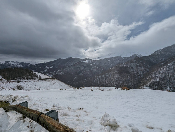 Zimní krajina: Hory oblečené v bílém pod mrznoucí, zataženou oblohou, se silnicí a lesem na cestě - Fotografie, Obrázek