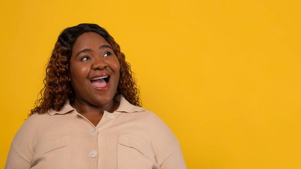 Περίεργος παχουλός χιλιετή μακριά μαλλιά σγουρά μαύρη γυναίκα φορώντας μπεζ πουκάμισο κοιτάζοντας κενό χώρο αντίγραφο για διαφήμιση και αναφωνώντας, ελέγξτε ωραία προσφορά, κίτρινο φόντο, web-banner - Φωτογραφία, εικόνα