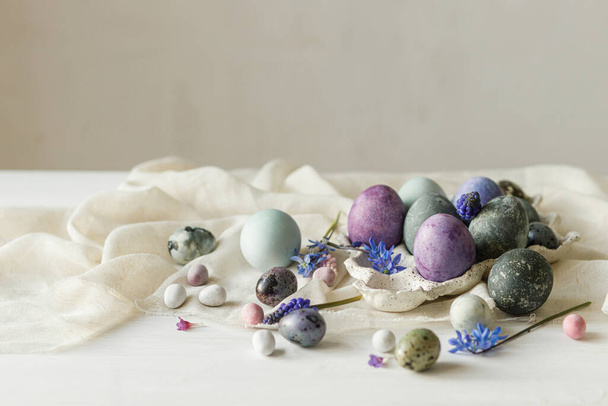 Stijlvolle paaseieren in modern dienblad, zachte lentebloemen en linnendoek op rustieke witte tafel. Vrolijk Pasen! Natuurlijk geschilderd marmer en paarse eieren stilleven. Seizoenen begroetingen - Foto, afbeelding