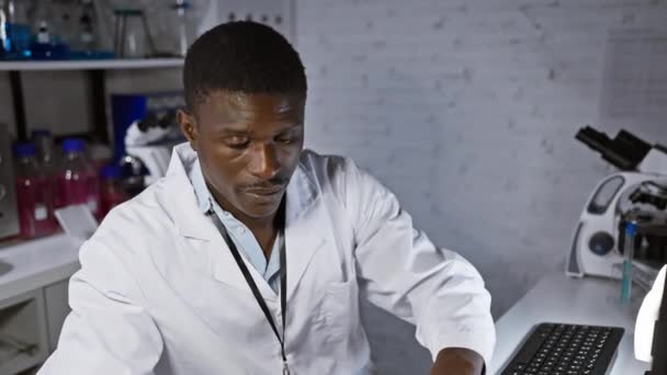 Científico africano enfocado en bata de laboratorio usando computadora en laboratorio moderno - Imágenes, Vídeo