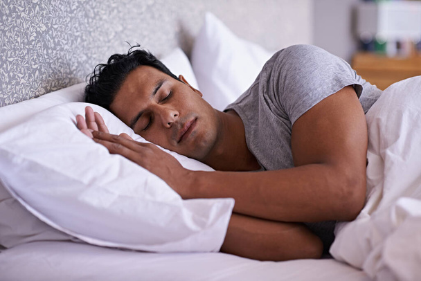 Muž, péče a spaní v posteli v dopoledních hodinách, unavený a klid odpočívat na měkkém polštáři s pohodlnou matrací. Zdravá osoba, snít nebo relaxovat v moderní ložnici, líný víkend nebo únava nebo wellness doma. - Fotografie, Obrázek