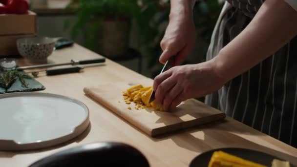 Oříznutý záběr nerozpoznatelného kuchaře krájejícího kukuřici na dřevěné desce na kuchyňském stole v kuchyni - Záběry, video