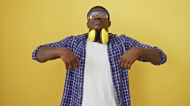 Attractive african american man finding zen, meditating in yoga pose with closed eyes, safety glasses on, against yellow isolated wall. embrace the calm life concept - Footage, Video