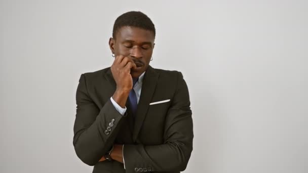 Hombre afroamericano estresado en traje, de pie aislado con mirada nerviosa, mordiendo las manos en ansiedad sobre fondo blanco - Imágenes, Vídeo