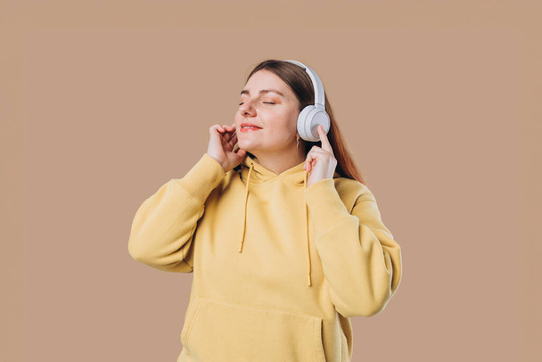 Profile portrait of charming woman in massive headphones listening to music on isolated background. Happy girl in hoodie smiles. - Photo, Image