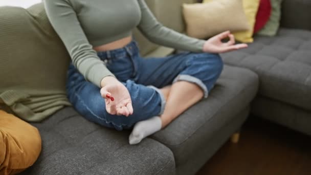 Klidná žena medituje na pohovce v útulném obývacím pokoji s barevnými polštáři, ztělesňující bdělost a klid. - Záběry, video