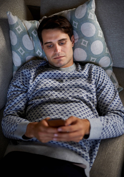 Home, night or above of man on a phone for social media blog, post or network on a sofa. Streaming movie, mobile app or person online for texting on technology for article, email or news to relax. - Photo, Image