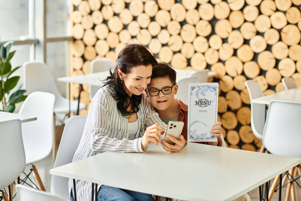donna allegra in abiti accoglienti con il figlio con la sindrome di Down guardando il menu sullo smartphone - Foto, immagini