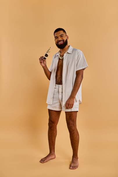 A stylish man in a white shirt and shorts strikes a pose while confidently holding a pipe in his hand. - Fotoğraf, Görsel