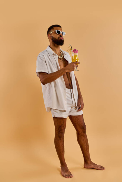 Un uomo elegante in camicia bianca e pantaloncini gode di un drink rinfrescante in un ambiente sereno, trasudando relax e soddisfazione. - Foto, immagini