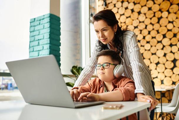 alegre madre pasar tiempo con su hijo con síndrome de Down en la cafetería mientras juega en el ordenador portátil - Foto, imagen