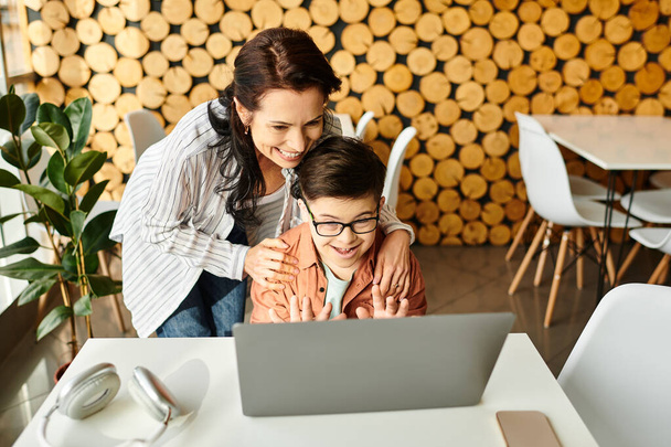 красивая веселая мать смотрит на ноутбук с ее включительно милый сын с синдромом Дауна в кафе - Фото, изображение