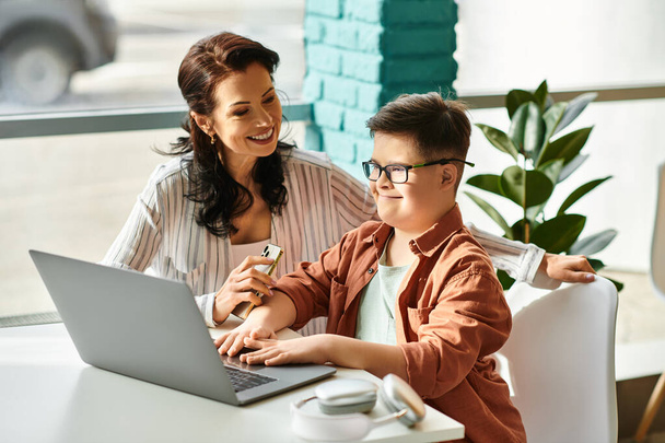 adorable garçon inclusif avec trisomie 21 passer du temps avec sa mère joyeuse devant un ordinateur portable - Photo, image